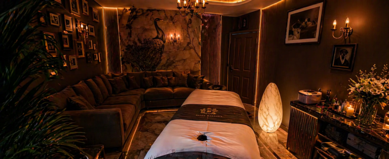 Luxurious spa treatment room with a massage table, a large sectional sofa, warm amber lighting, wall art, and candles.